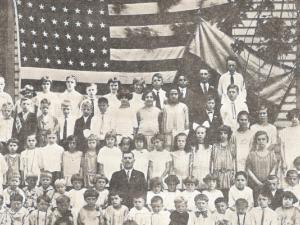 A large group of youth and adults standing in front of a large American flag and a smaller Ukrainian one.