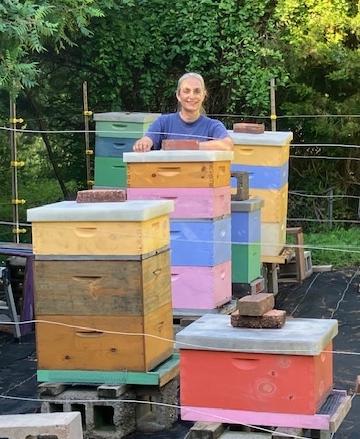 Cathy Blumig standing amid colorfully-painted beehives