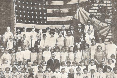A large group of youth and adults standing in front of a large American flag and a smaller Ukrainian one.