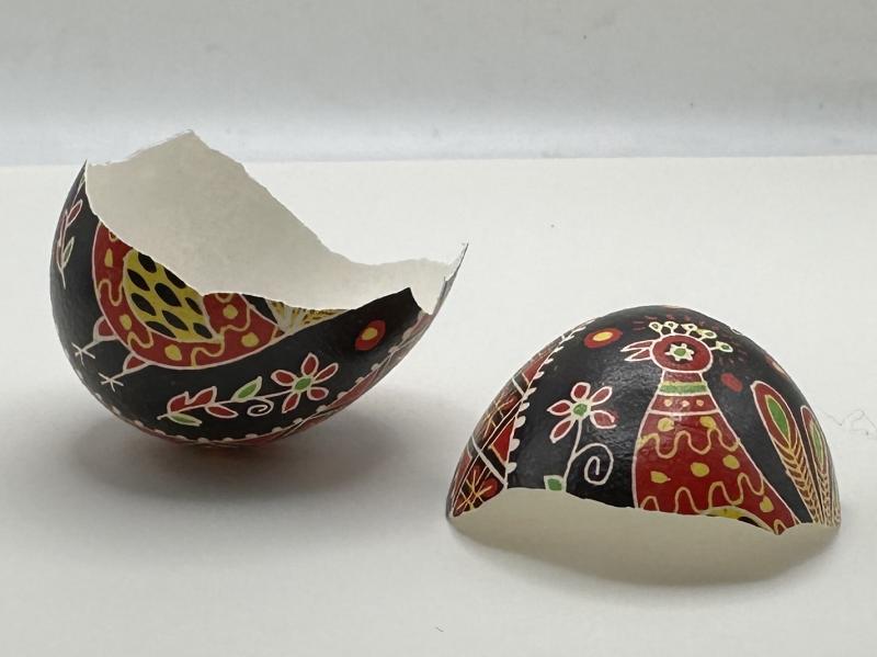 A broken pysanka with a red and yellow chicken pattern