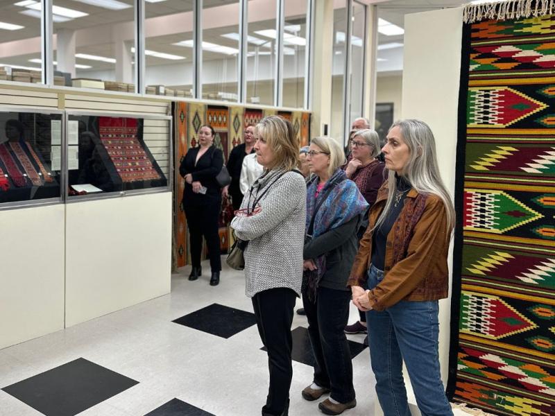 A group of adults in a gallery space with colorful weavings listening to a tour guide.